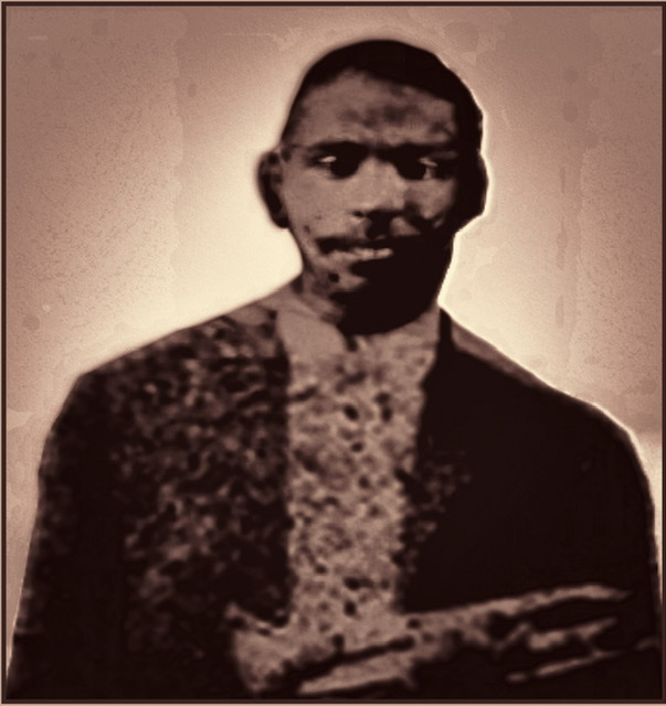 A retouched closeup with colored golden sand browns background of a cutout from the only known black and white photograph of Buddy Bolden's of his head and torso from the waist up holding trumpet at his waist.