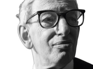 A black and white reversed photograph of a headshot of a middle-aged Eric Hobsbawm wearing glasses.