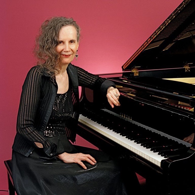 A full color photograph of Joanne Brackeen late in her career sitting royally at piano.