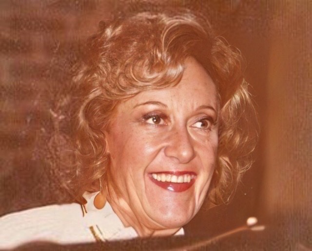 An enhanced color photograph of a middle-aged smiling Marian McPartland's head wearing red lipstick💄turned towards her left.