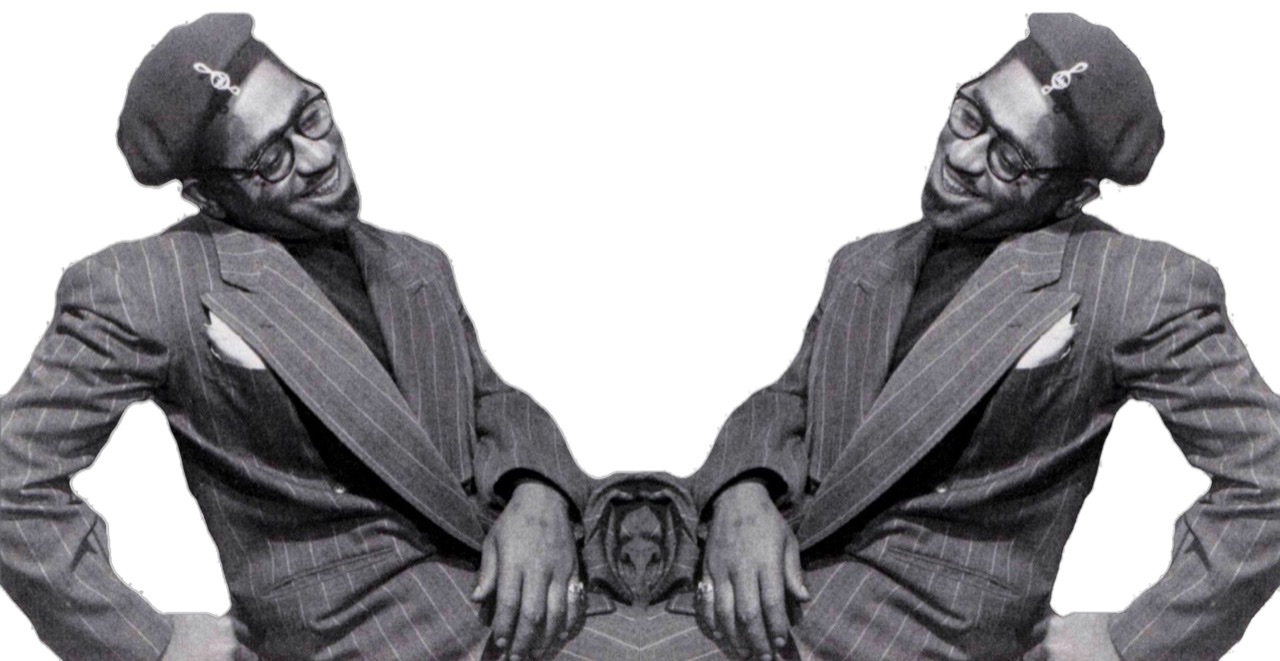 Dizzy Gillespie leaning back to left and smiling while seated in a gray pin-striped suit.
