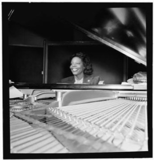 A William P. Gottlieb photograph of Mary Lou Williams with a grand piano fretboard in foreground.