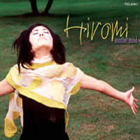 The album cover for "Another Mind" by Hiromi Uehara with her standing with her arms outstretched wearing a patterned yellow scarf.