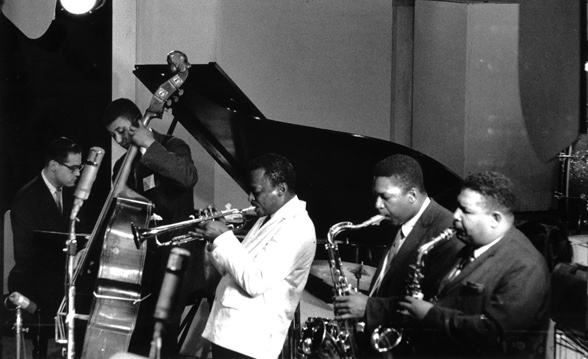 A black and white photograph of the 1959 Miles Davis Sextet with Bill Evans at piano, Paul Chambers on bass, Miles on trumpet, John Coltrane on tenor saxophone, and Cannonball Adderley on alto saxophone.  Drummer Jimmy Cobb is not seen in photograph.