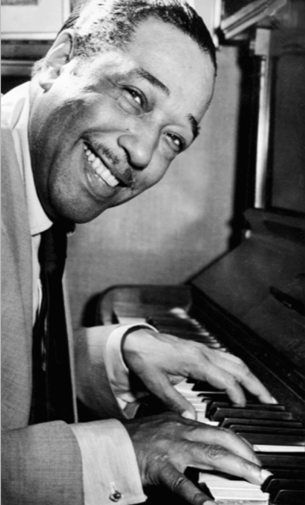 A black and white photograph of Duke Ellington facing right in profile sitting bent over the piano with a big smile turned towards the camera and his hands on the keyboard 🎹.