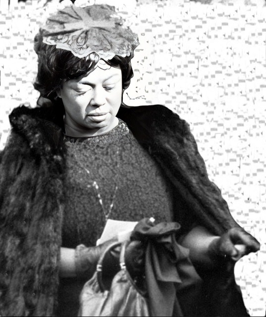 A black and white photograph of a heavyset Hazel Scott in late middle age wearing a fur coat and carrying a leather double handle handbag.