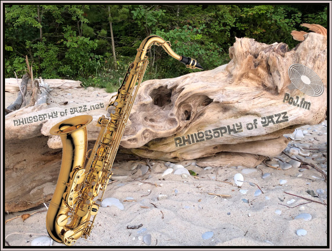 A closeup photograph of a large piece of driftwood appearing to have engraved PoJ.fm logos burned into the wood and a large shiny gold tenor saxophone leaning prominently up against the driftwood on the left side at a 22.5° angle.
