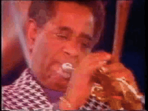 Dizzy Gillespie in color and in slow motion blowing his trumpet with huge expanding cheeks.