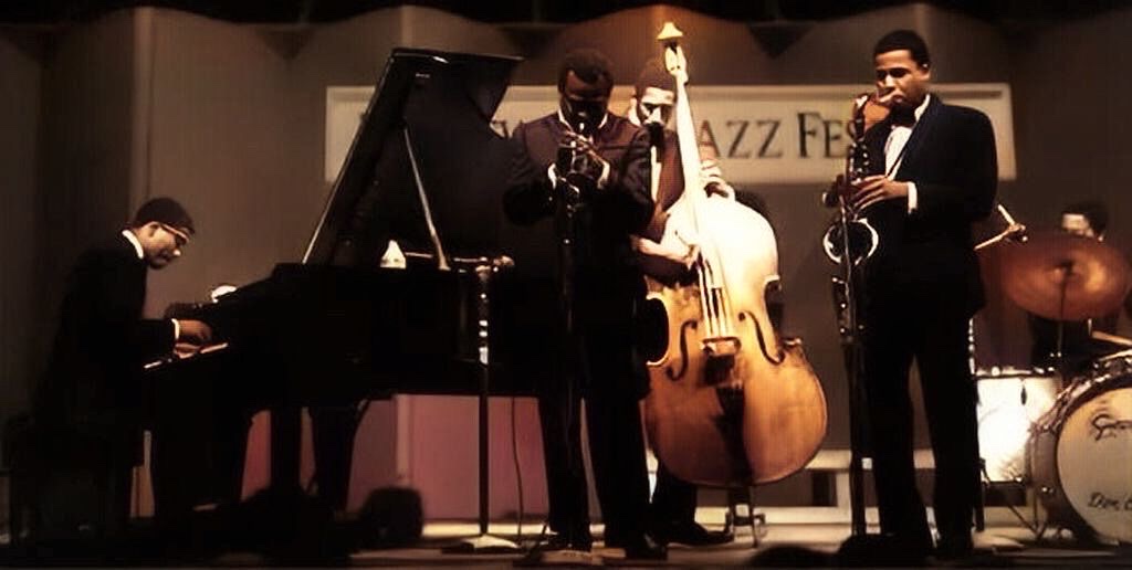 A colorized photograph of the second great Miles Davis quintet performing on stage at the Newport Jazz Festival in 1967.