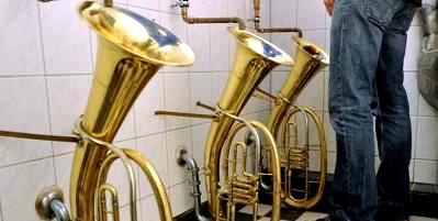 A color photograph of three highly polished Wagner tubas with bells pointed upward being used as urinals in a pub in Freiburg, Germany.
