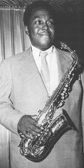A black and white photograph of Charlie Parker facing right and smirking.