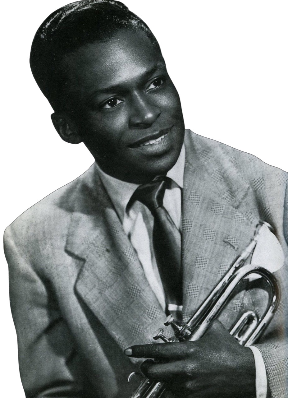 A cutout photo of Miles Davis as a young man wearing a sports jacket and smiling while holding his trumpet down by his left side.